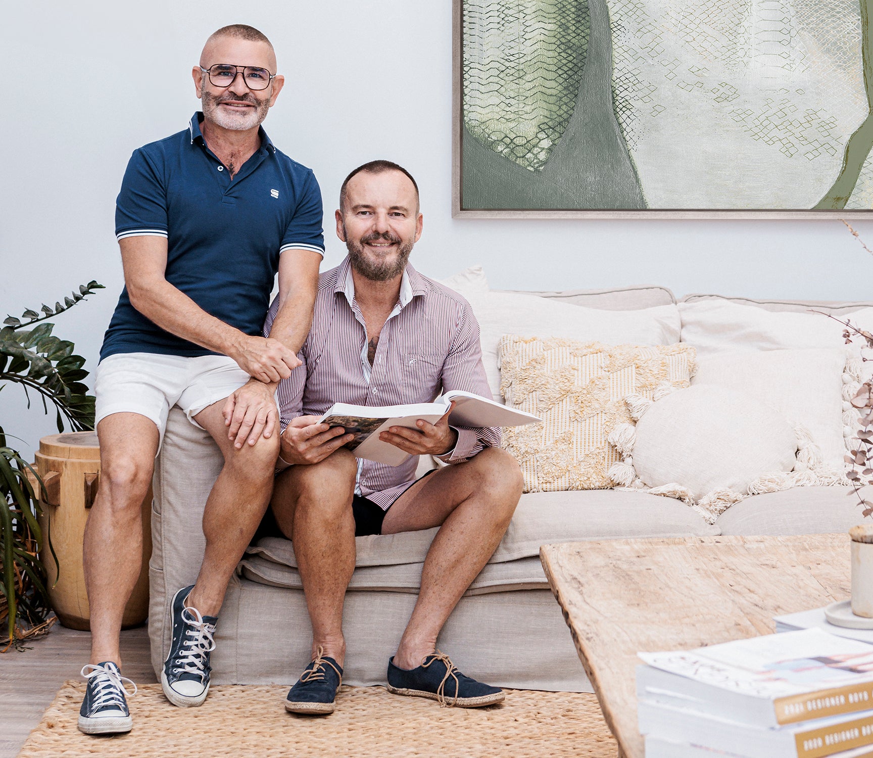 Photo of Gavin and Warren, the founders of Designer Boys, sitting on a beige couch and looking at a Designer Boys Catalogue.